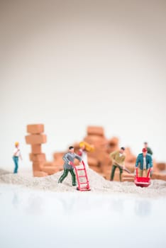Miniature workmen doing construction work on a cloudy day with the overcast sky like background
