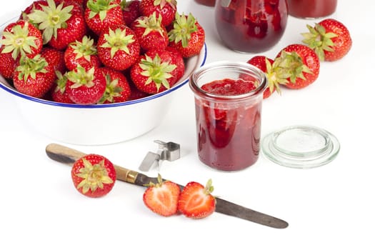 Strawberry jam in jars and fresh strawberries in a bowl against a white background