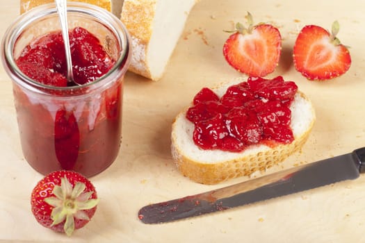 Homemade strawberry jam on white bread and a glass of strawberry jam on a wooden board