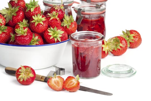 Homemade strawberry jam and fresh strawberries in jars against a white background
