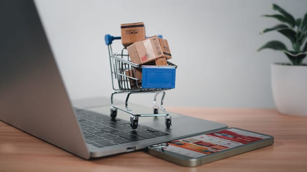 Shopping cart and product boxes placed on laptop computer represent online shopping concept, website, e-commerce, marketplace platform, technology, transportation, logistics and online payment concept.