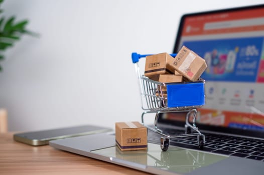 Shopping cart and product boxes placed on laptop computer represent online shopping concept, website, e-commerce, marketplace platform, technology, transportation, logistics and online payment concept.