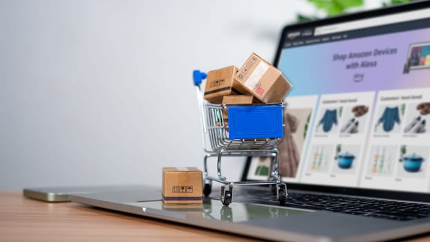 Shopping cart and product boxes placed on laptop computer represent online shopping concept, website, e-commerce, marketplace platform, technology, transportation, logistics and online payment concept.