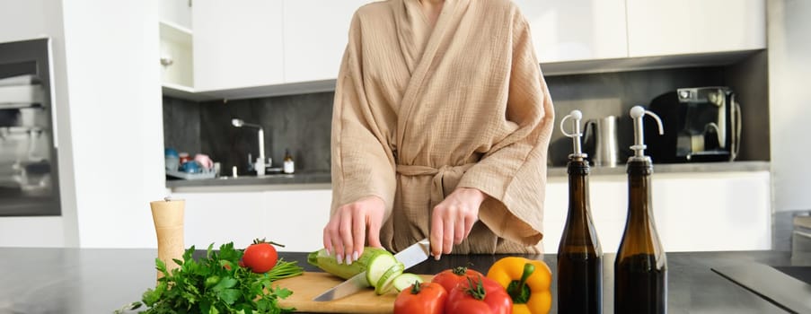 Close up portrait of female hands, woman wearing robe, cutting vegetables on chopping board, cooking vegan dinner, vegetarian meal for family, standing in kitchen.