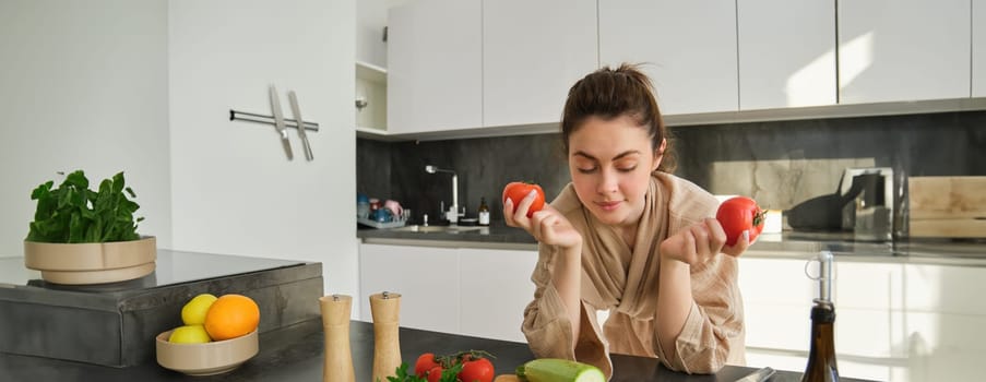 Portrait of woman cooking at home in the kitchen, holding tomatoes, preparing delicious fresh meal with vegetables, standing near chopping board.