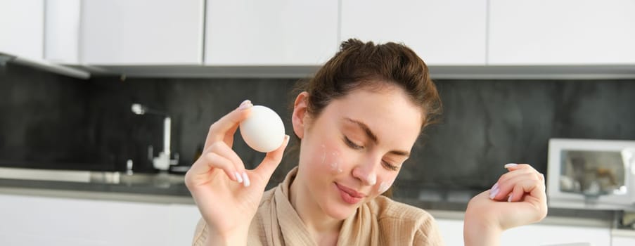 Attractive young cheerful girl baking at the kitchen, making dough, holding recipe book, having ideas.