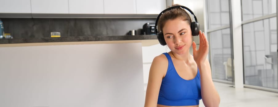 Portrait of beautiful sportswoman puts on wireless headphones, workout at home, listens to music to focus on yoga session.