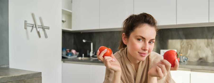 Portrait of beautiful woman cooking in the kitchen, chopping vegetables on board, holding tomatoes, lead healthy lifestyle with preparing fresh salads, vegan meals.