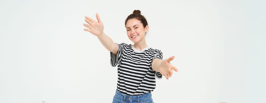 Portrait of cute smiling woman stretches her hands, reaches to hold something, wants to hug you, standing over white background.