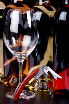 Wine glass,corkscrew with precious wood handle and wine bottles against a black background