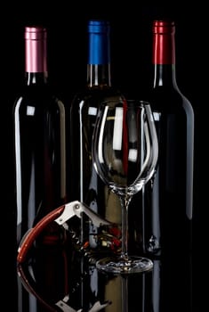 Three bottles of wine,a wine glass,and corkscrew on a black reflective background