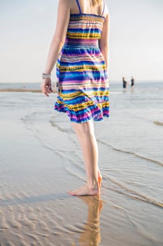 Yong woman in dress walking on sea shore