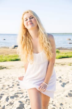 Smiling woman wriggles in white dress at beach
