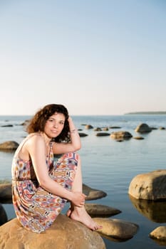 Young woman barefoot sitting at stone at evening