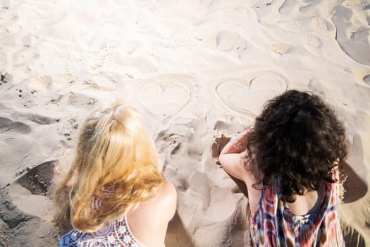 Two young womans draw hearts on warm sand