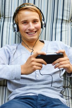 Young male chilling out to music and playing hand-held game