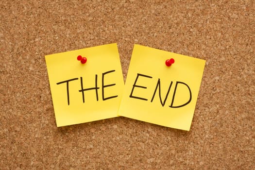 The End written on two yellow sticky notes on an office cork bulletin board.