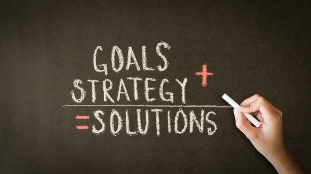 A person drawing and pointing at a Goals, Strategy, Solutions chalk drawing