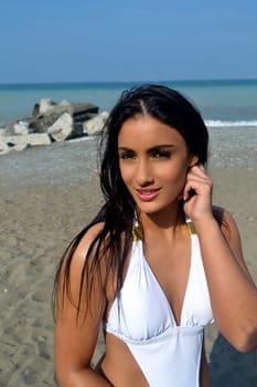 A closeup picture of a beautiful young woman in a white bikini, with her.long black hair, standing on the beach on lake Ontario..