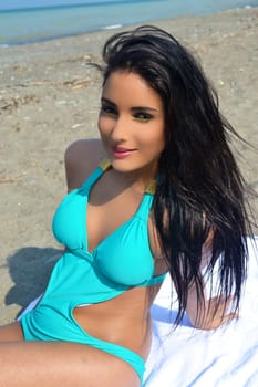 A lovely teen girl in a turquoise bikini sitting on the beach on lake Ontario.with her long black hair, sunbathing, in a closeup picture..