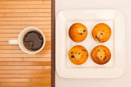 Vanilla with chocolate chips Muffins on a white plate with  a cup of coffee.