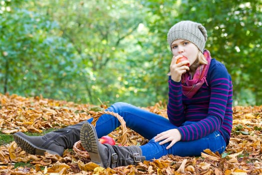 young girl eating red apple in autumn garden