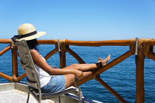 Young woman sitting on a balcony looking over the ocean enjoying the view