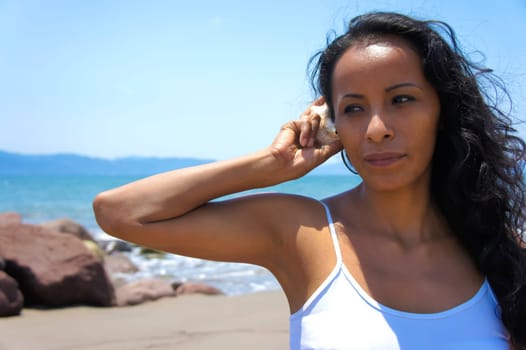 Youg latina woman listening to the sound of a shell.