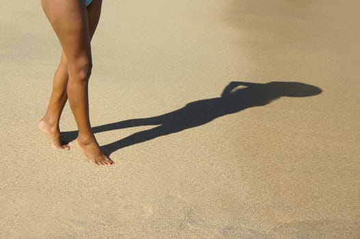 A woman walking on the beach casting a silhouette shadow.