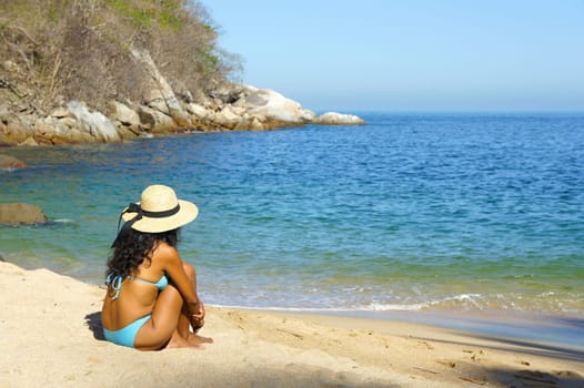 Young woman sitting at the beach looking over the ocean. .