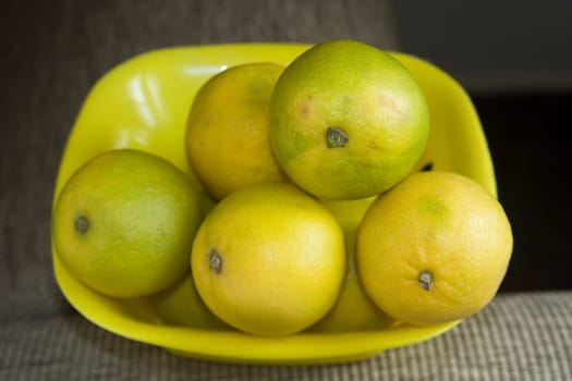 Yellow and greenish sweet lemons placed in yellow plastic tray