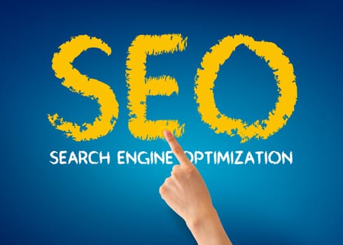 Hand pointing at a Search Engine Optimization word on blue background.
