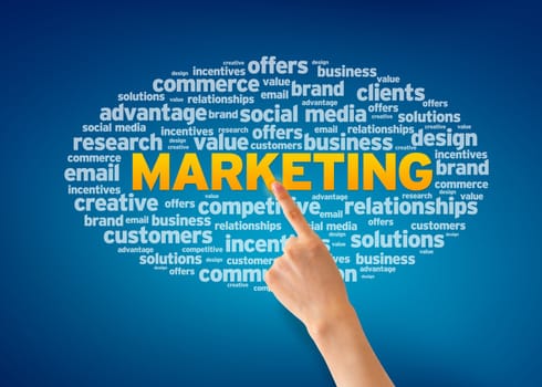 Hand pointing at a Marketing word cloud on blue background.