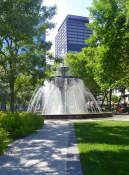 Downtown Hamilton, Canada, with a nice fountain and trees, benches,.with high rises in the background..
