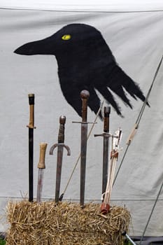 Swords in front of a tent wall painted with a raven