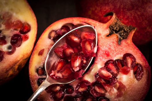 Pomegranate fruit on a old wooden table with a silver spoon.