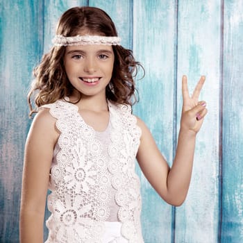 Brunette happy hippie children girl smiling with peace hand sign on blue wood