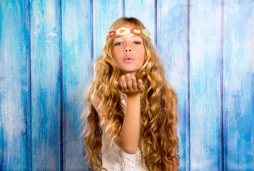 Blond hippie children girl blowing mouth with hand on blue grunge wood
