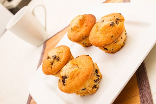 Vanilla with chocolate chips Muffins on a white plate with  a cup of coffee.