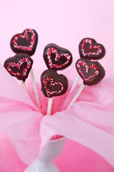 Heart shaped chocolate dipped cakepops with sprinkles on a pink background