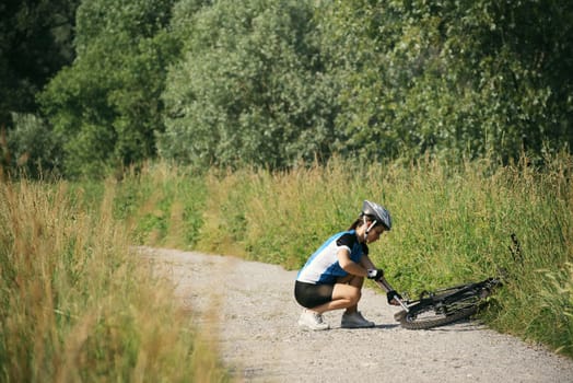 young woman training on mountain bike and repairing flat tyre on track in countryside