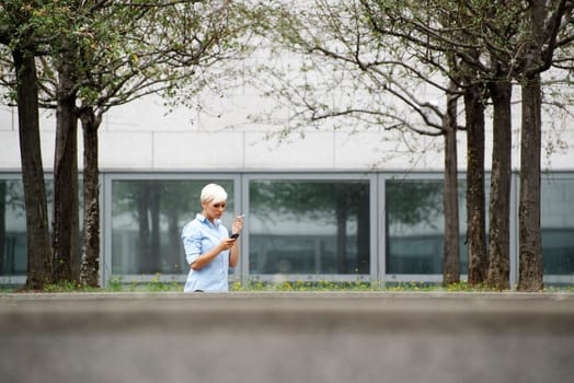 young businesswoman smoking cigarette during break out of office building. Wide shot, copy space