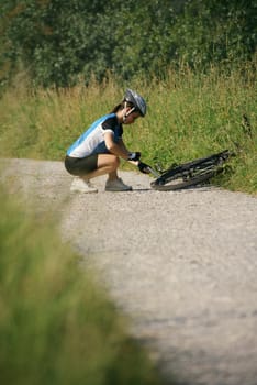 young woman training on mountain bike and repairing flat tyre on track in countryside