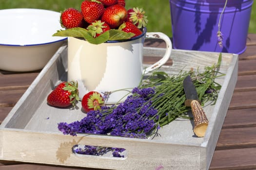 Fresh strawberries and freshly cut lavender lie on a wooden tray