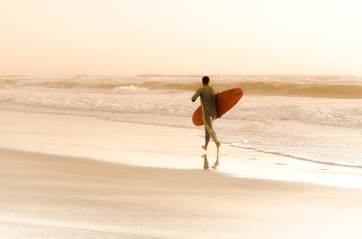 Surfer running on the beach with the waves at sunset in Portugal.