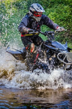 Quad rider through water stream in the forest.