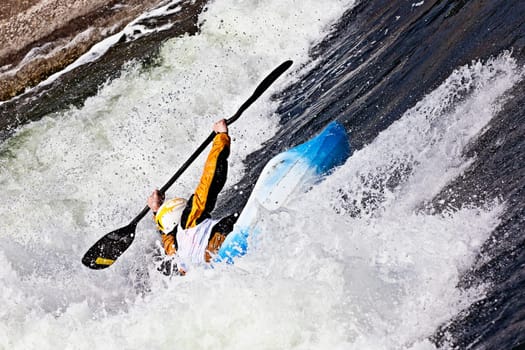 an active male kayaker rolling and surfing in rough water