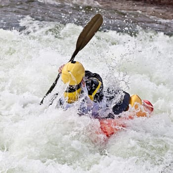 an active male kayaker rolling and surfing in rough water