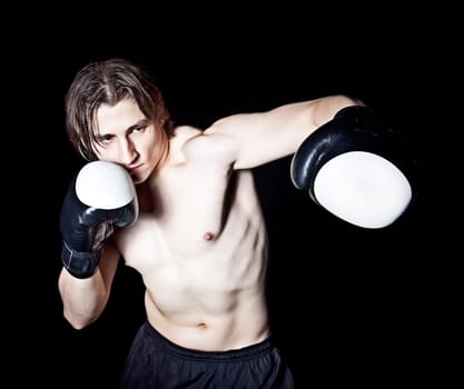 Young caucasian man boxing with gloves on black background