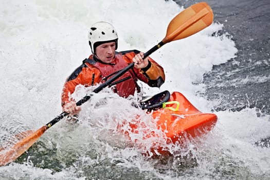 an active male kayaker rolling and surfing in rough water
